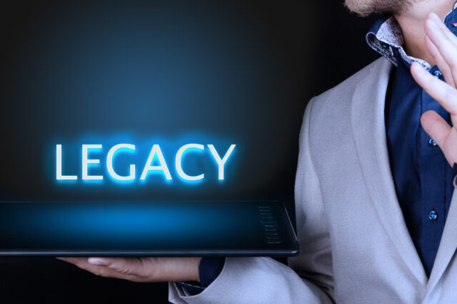 Businessman, man holds in his hand a tablet with a neon word, LEGACY text. Business concept.